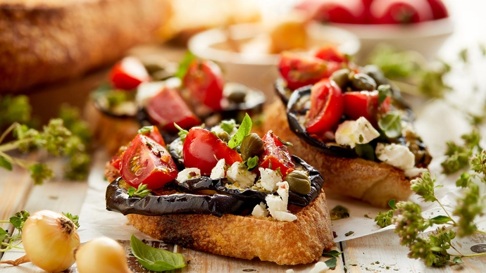 A plate of bruschetta surrounded by fresh herbs, bread and vegetables