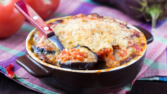 A large black bowl of vegetable moussaka with a serving spoon