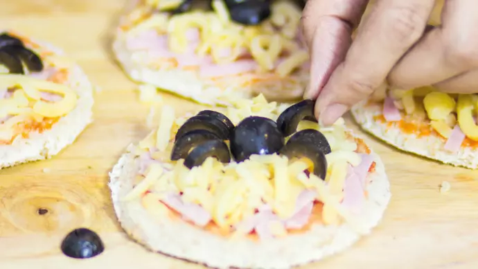 Preparation of a mini pizza topped with cheese, tomato sauce, ham and olives