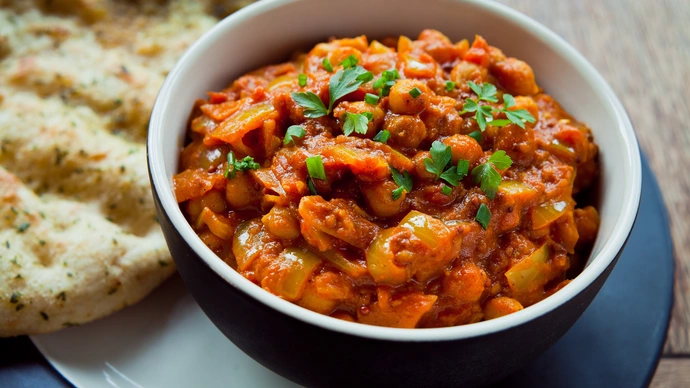 Bowl of vegetable curry which includes chickpeas and naan bread on the side