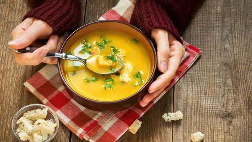 Hands in gloves, one holding a spoon and the other holding a bowl of lentil soup