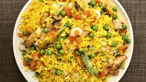 A vibrant bowl of yellow rice paella with garden peas and other assorted vegetable pieces