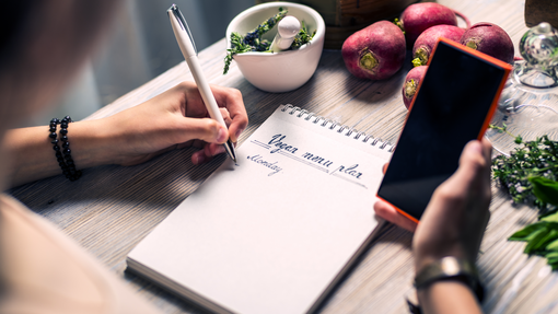 A person using a phone and notepad to write a meal plan