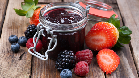 a jar of thick purple berry jam surrounded by an assortment of fresh berries