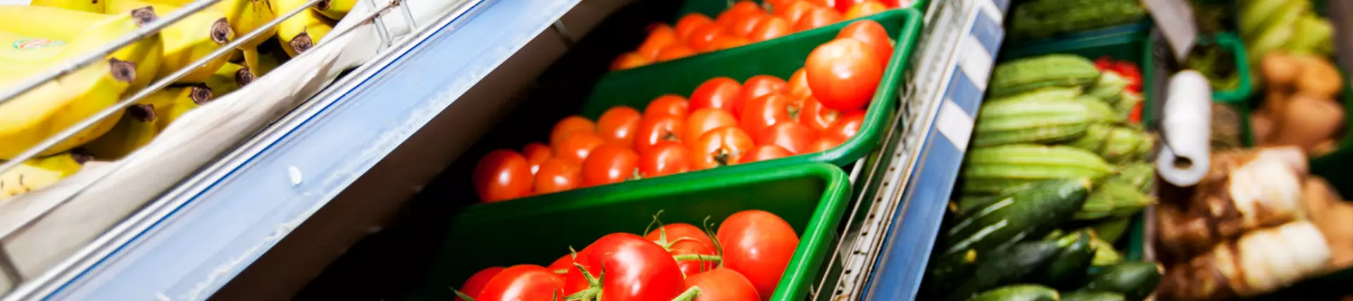 A photo of trays of bananas, tomatoes and lettuce displayed in a supermarket aisle.